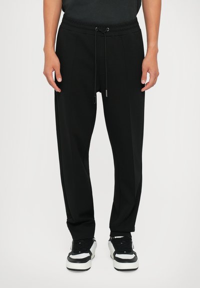 Sorte joggingbukser i blødt stof, med en snor i taljen, sidelommer og en afslappet pasform. Båret med sort og hvide sneakers.