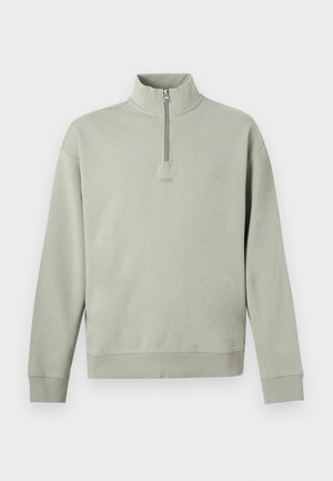 Ανοιχτό πράσινο πουλόβερ με μακριά μανίκια, ψηλό γιακά και μικρό φερμουάρ, με διακριτικό κείμενο "HUGO" στο στήθος.