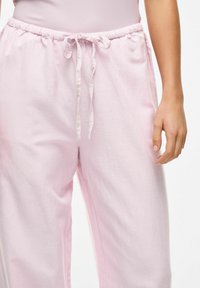 Pantalons de lounge en tissu doux de couleur rose clair avec une taille élastique et un lien à nouer. Présente une coupe décontractée et une texture lisse.