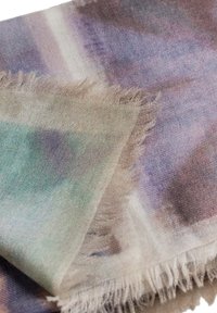 Sciarpa morbida e leggera con una combinazione di colori che includono verde, viola e beige. I bordi sono frangiati per aggiungere texture e dettaglio.