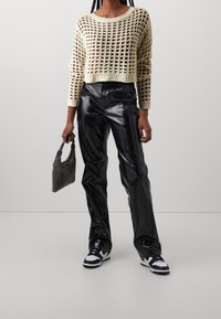 Sweter z dzianiny w kolorze kremowym o otwartym splotem, zestawiony z błyszczącymi czarnymi spodniami z ekoskóry. Akcesoria obejmują torebkę o fakturowanej powierzchni w kolorze czarnym.