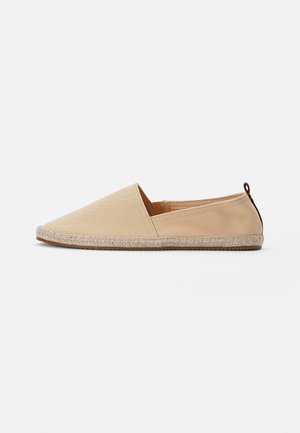 Beige instapschoen espadrille met gevlochten jutezoolrand en een bruine trek-lus bij de hiel, zijaanzicht op een witte achtergrond.