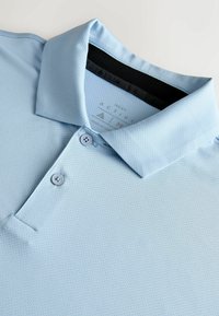 Polo bleu clair texturé avec deux boutons et un col replié sur un fond clair.