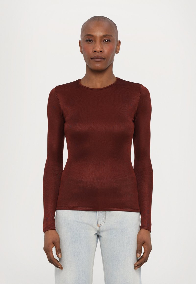 Bordeauxrotes Langarmoberteil mit enganliegendem Design, rundem Ausschnitt und geripptem Material, kombiniert mit hellblauen Jeans.