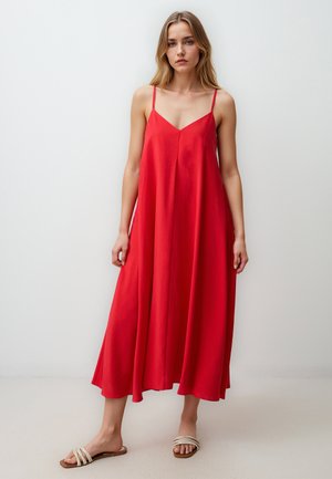 Rotes ärmelloses Maxikleid mit V-Ausschnitt, fließender Silhouette und leichtem Stoff. Kombiniert mit weißen Sandalen mit Riemchen.