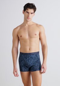 Tengerészkék boxer alsónadrág, textúrált, absztrakt mintával, sötét derékrésszel, amelyen a "BJÖRN BORG" felirat szerepel. Az anyag lágy és rugalmas.