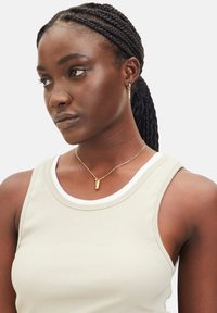 Ribbet beige tanktop med hvid kant, parret med en guldkæde med en lille vedhæng. Detalje af fletninger.