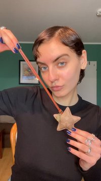 Μπρελόκ σε σχήμα αστεριού από υφή μπεζ δέρμα με καφέ λουράκι· διαθέτει μια μικρή χρυσή διακοσμητική λεπτομέρεια.