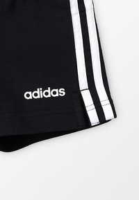 Pantalones cortos deportivos negros con rayas blancas en los laterales, que cuentan con un tejido suave y elástico y un logo blanco de Adidas cerca del dobladillo.