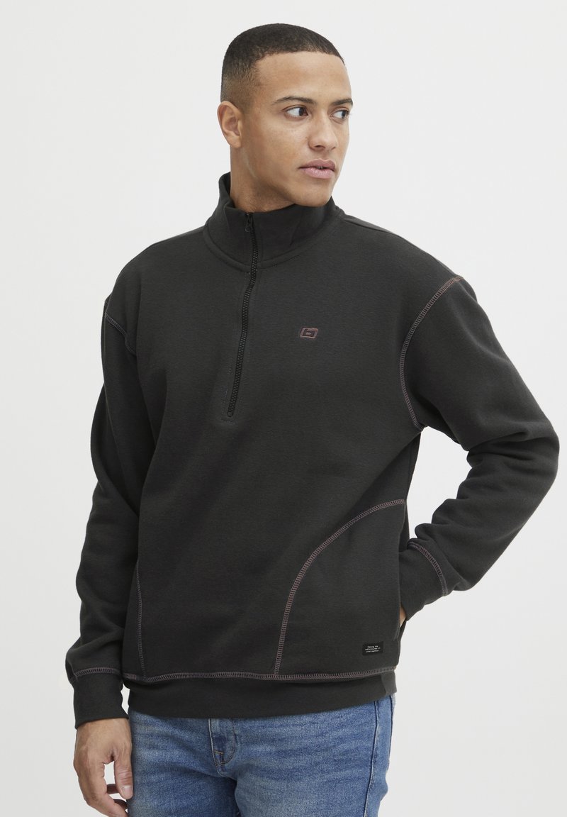 Must värvi fleece-sweater neljandiku tõmbeteki ja kontrastsete õmblustega, millel on rinnal väike logo ja lõtv lõige.