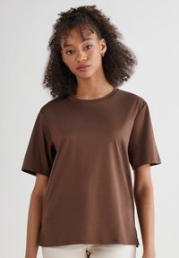T-shirt marrone a maniche corte con scollatura rotonda, realizzato in tessuto morbido, caratterizzato da una vestibilità rilassata e uno spacco laterale per il comfort.