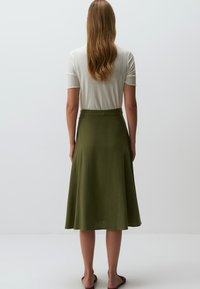 Jupe verte en ligne A, fabriquée dans un tissu léger et texturé, avec une taille ajustée et un ourlet fluide. Complétée par un haut simple à côtes.
