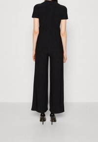 Svart jumpsuit med korta ärmar, insnörd midja, vida ben och mjuk textur. Bärs med svarta klackskor.