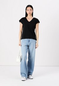 Svart V-hals t-shirt med korta ärmar, i kombination med ljusblå flarejeans och vita sneakers. Modellen håller en liten vit handväska.