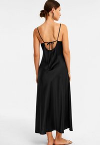 Schwarzes Satin-Maxikleid mit dünnen Trägern, das einen tiefen Rückenausschnitt und eine Bindeschließe aufweist. Glatte Textur und ein fließendes Design, das bis zu den Knöcheln reicht.