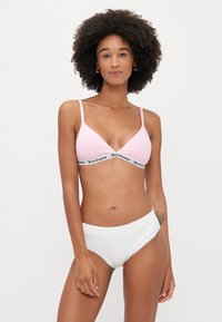 Gaiši rozā bralette ar regulējamiem siksniņām un melnu zīmolu elastīgo jostu. Balti augstvērtīgi bikini apakšdaļa, gluda tekstūra, vienkāršs dizains.