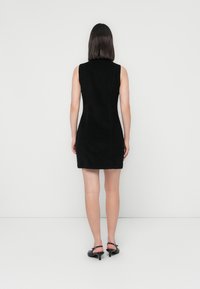 Robe noire sans manches en tissu texturé, au design ajusté et longueur au-dessus du genou, avec un subtil détail de couture à l'arrière.