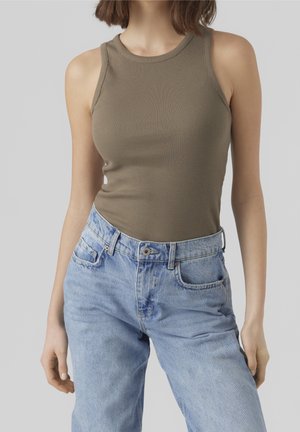 Femme portant un haut sans manches côtelé vert olive et un jean en denim taille haute bleu clair sur fond uni.