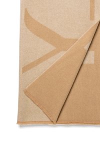 Beige deken met een geometrisch patroon in een lichtere tint. Zachte textuur met franjes aan de randen; gedeeltelijk gevouwen om de onderzijde te tonen.