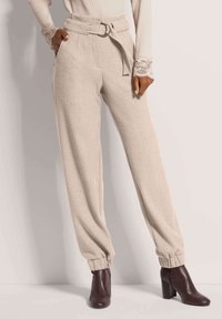 Beige hochtaillierte Hose mit einem Gürtel und einer runden Schnalle, mit umgeschlagenen Knöcheln und einer weichen Textur, kombiniert mit dunklen, hohen Stiefeletten.