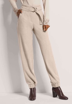 Beige hoge taille broek met een riem met een ronde gespsluiting, opgerolde enkels en een zachte textuur, gecombineerd met donkere, hakschoenen tot de enkels.