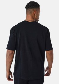 Camiseta de algodón negra con mangas cortas, corte relajado y cuello redondo. La parte trasera presenta un diseño liso sin impresiones ni logotipos visibles.