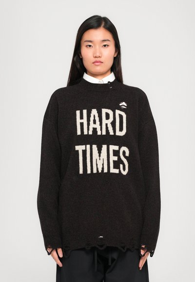 Maglione oversized marrone scuro con testo bianco in grassetto "HARD TIMES", colletto rotondo, vestibilità ampia e bordi inferiori sfilacciati.