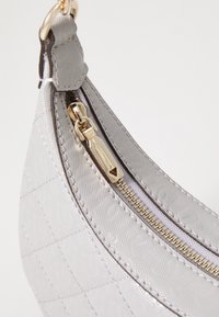 Grå tekstureret håndtaske hjørne med gylden lynlås og remring, syede detaljer og subtil monogrammønster på glat stof.