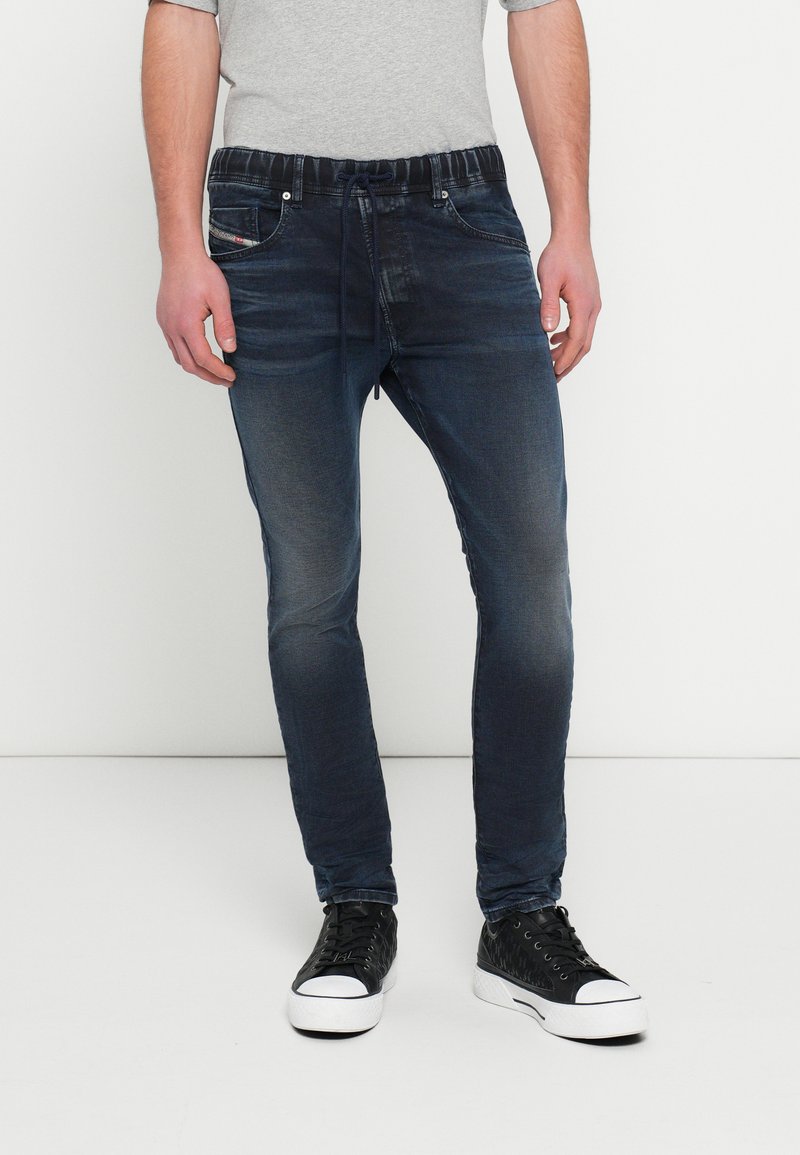 Meeste tumedat sinist teksapükse, millel on nööriga vöökoht, kitsenev lõige ja kaks esitaskut. Kandmisel mustad tossud ja hall särk.