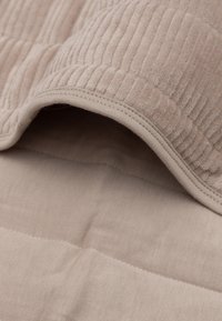 Couverture beige texturée avec un design à côtes, présentant une douce couche supérieure en velours et un dessous en coton lisse, partiellement repliée sur elle-même.