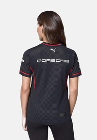 Czarna koszulka z krótkim rękawem z wzorem w kratkę, czerwonymi akcentami oraz białym logo "PORSCHE" z tyłu. Teksturowana tkanina o sportowym designie.