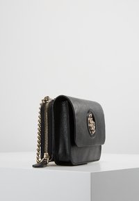 Sort læderhåndtaske med en fold-over klap, gylden kædetræk, lynlåslomme på siden og præget logo på forsiden. Kompakt og struktureret design.