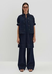 Dark denim outfit featuring a short-sleeve button-up shirt with a pocket and wide-leg trousers. Contrast stitching details and minimal design.