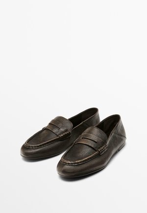 Mocassins en cuir marron foncé avec une texture lisse, des coutures décoratives et une sangle décorative sur le devant. Design à profil bas.