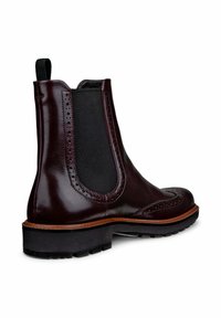 Bottines Chelsea en cuir bordeaux avec panneaux élastiques sur les côtés, détails de brogue décoratifs et semelle en caoutchouc noir texturé.