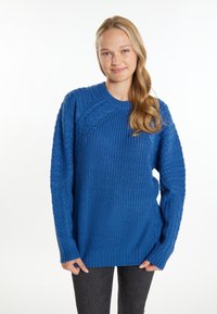 Maglione azzurro a maglia con motivi testurizzati, colletto a girocollo e maniche lunghe con polsini a coste. Indossato sopra jeans scuri.