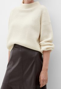 Suéter de punto acanalado en color crema con cuello alto y mangas enrolladas, combinado con una falda de cuero marrón oscuro con detalles de costura.