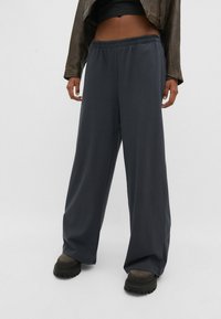 Pantalones anchos de color gris oscuro hechos de material suave con una cintura elástica, que presentan una textura lisa y un ajuste relajado, combinados con calzado negro grueso.