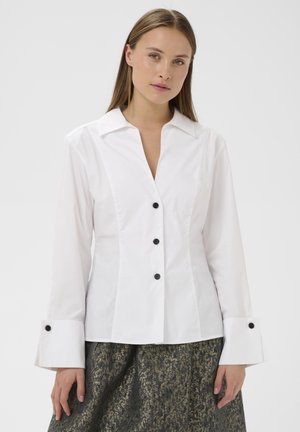 Chemise blanche à manches longues avec un design ajusté, cols pointus et boutons noirs, dotée de larges poignets avec des accents de boutons assortis.