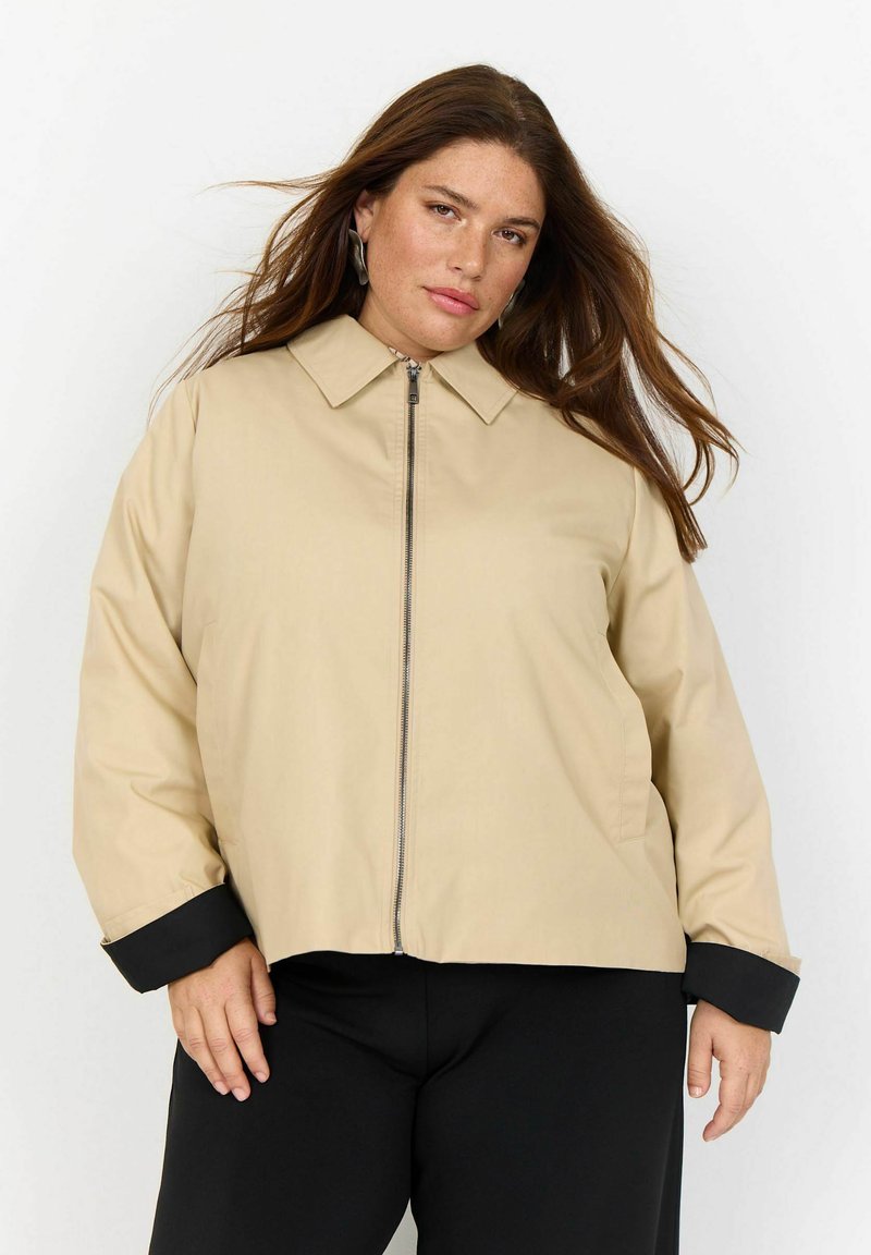 Bežna zip-up jakna s ovratnikom, črnimi manšetami in sproščenim krojem. Gladek material z lahkotnim in sproščenim dizajnom.