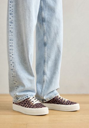 Leopard print canvas sneakers with white rubber soles, paired with loose light blue denim jeans, showcasing a relaxed fit and visible stitching.
