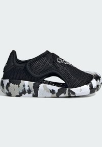 Scarpa slip-on nera in mesh con design aperto, caratterizzata da una suola testurizzata multicolore con motivo camouflage nei toni del nero, bianco e grigio.
