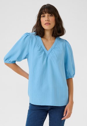 Blouse bleu clair texturée avec des manches courtes bouffantes et un décolleté en V. Le tissu possède un motif froissé subtil, offrant une coupe décontractée.