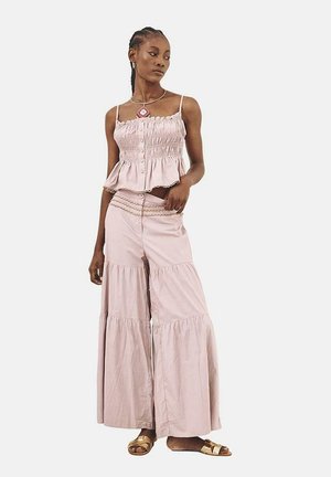 Top corto de color rosa claro, con volantes y detalles de botones; pantalones anchos a juego con dobladillo con volantes; estilizado con sandalias planas doradas.