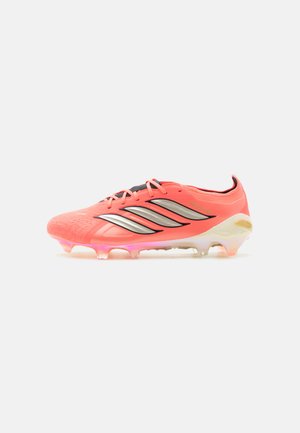 Chaussure de football corail vif avec des rayures argentées, un système de laçage et une semelle translucide à crampons, vue de côté sur un fond blanc.