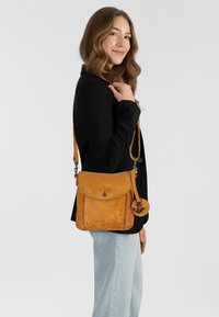 Borsa a tracolla gialla in pelle con chiusura a patta, caratterizzata da un dettaglio hardware a forma di ancora e un accento di portachiavi rotondo. Tessuto morbido.