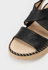 Sorte lær sandaler med to brede remmer, beige fotseng og flettet svart og beige såle. Har en glatt tekstur og subtil søm.