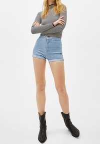 Höga denimb shorts i ljusblått, med en klassisk femficksdesign och knappstängning. Kli av en svart och vit randig långärmad topp.