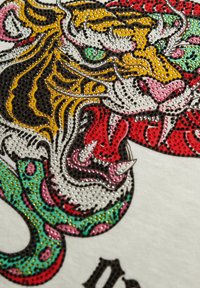 Kolorowa sztuka przedstawiająca szczegółowy wzór tygrysa i węża, ozdobiona małymi, błyszczącymi cyrkoniami na teksturowanym tle.