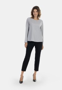 Világosszürke, hosszú ujjú felső, kerek nyakkivágással, fekete, slim fit nadrággal és tűsarokkal párosítva, fehér háttér előtt.